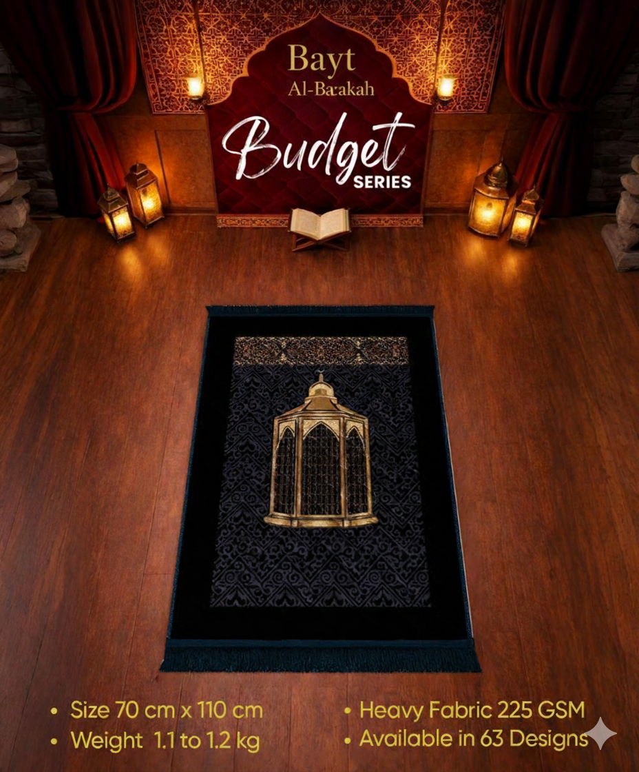 Black prayer mat with gold design on a wooden floor, featuring 'Bayt Al-Barakah' branding.